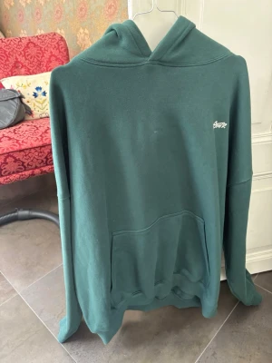Grön hoodie från Pull&Bear - Mörkgrön hoodie från Pull&Bear med vit logga på bröstet och stort tryck på ryggen. Perfekt för dig som gillar streetwear och vill ha en stilren men ändå unik look.