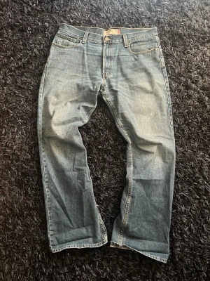 Levi's 527 bootcut jeans blå - Säljer ett par klassiska blå Levi's 527 jeans med bootcut-modell. Jeansen har fem fickor, gylf med dragkedja och knapp samt slitna detaljer för en avslappnad look. Perfekta för dig som gillar en lite vidare passform nertill.