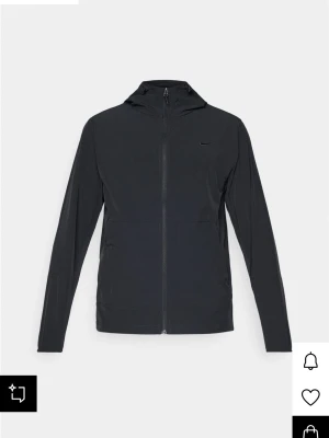 Svart vindjacka från Nike - Stilren svart vindjacka från Nike med hel dragkedja framtill och huva. Jackan har diskret Nike-logga på bröstet och är tillverkad i lätt, vindtätt material. Perfekt för blåsiga dagar och enkel att matcha med olika outfits. Nypris: 1050