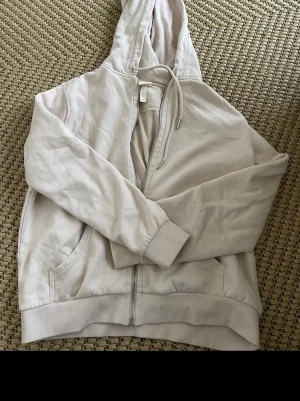 Ljusbeige hoodie med dragkedja H&M - Ljusbeige hoodie från H&M med dragkedja framtill, huva med dragsko och två fickor. Perfekt för en avslappnad stil. Tillverkad i mjukt material som känns skönt mot huden. (Oversized)