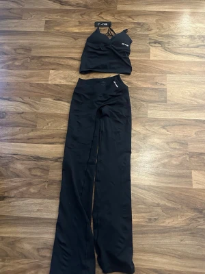 Svart set från OYSHO med topp & byxor - Säljer ett svart set från dfyne  med en croppad topp med smala axelband och matchande utsvängda byxor i stretchigt material. Perfekt för en trendig och bekväm look. Diskret logga på både topp och byxa. Har inte använt detta då det var för litet för mig. Det ska enligt kvittot vara marinblått men jag anser att det är mer svart 