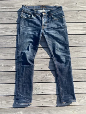 Mörkblå jeans från Nudie Jeans - Ett par riktigt snygga Nudie Jeans med fet tvätt och klassisk look! Modellen är Grim Tim. Passar riktigt bra till en skjorta eller hoodie nu till sommaren☀️ Oanvända helt utan defekter! Kom gärna med bud eller frågor!🙌⭐️  Mått enligt sista bilden:   Ben längd: 101cm Innerbenssöm: 75cm Midja: 42cm