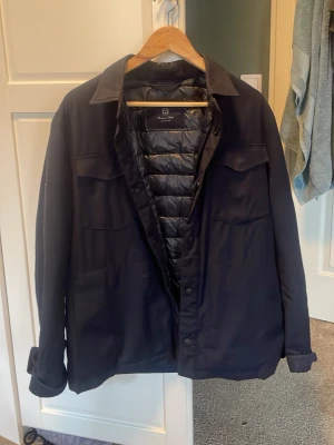 Mörkblå overshirt från Massimo Dutti - Stilren mörkblå overshirt från Massimo Dutti med quiltat foder. Sitter som bra på M med.Klassisk krage, två bröstfickor med lock och knäppning framtill. Perfekt lager-på-lager-plagg i ett mjukt och slitstarkt material. Snygg och enkel att matcha till olika outfits.