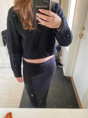 Svart croppad hoodie - En svart croppad hoodie med långa ärmar och huva. Hoodien har en enkel och stilren design utan tryck eller logga, perfekt för en avslappnad look. Mjuk bomullskänsla och normal passform.