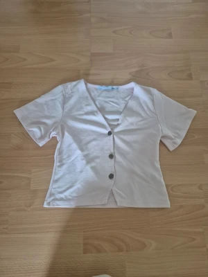 Rosa kortärmad topp med knappar - Snygg rosa topp med korta ärmar och v-ringning. Toppen har tre dekorativa knappar framtill och är tillverkad i mjukt bomullsmaterial. Enkel och stilren design som passar perfekt till jeans eller kjol.