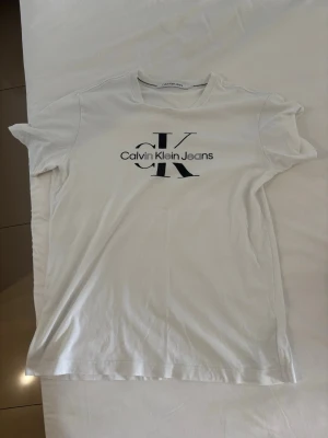 Vit Calvin Klein Jeans t-shirt - Vit t-shirt från Calvin Klein Jeans med klassisk logga i svart framtill. T-shirten har rund halsringning och korta ärmar. Tillverkad i mjuk bomull för en skön och avslappnad känsla. Ganska stor i storleken( typ Medium).
