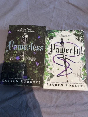 Powerless & Powerful av Lauren Roberts - Två böcker: 'Powerless' och 'Powerful' av Lauren Roberts. Omslagen är färgstarka med svärd, blommor och slingrande växter. Powerless har svart bakgrund med lila detaljer, Powerful har vit bakgrund med gröna och lila inslag. Perfekt för dig som gillar fantasy och romantik.