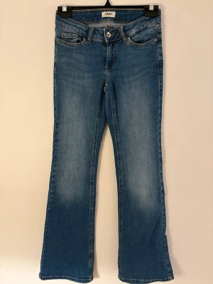 Blå bootcut jeans från ONLY - Snygga blå bootcut jeans från ONLY med klassisk femficksmodell och normalhög midja. Jeansen har en lätt tvättad look och är tillverkade i ett mjukt denimtyg som ger en bekväm passform. Perfekta till sneakers eller boots för en avslappnad stil.