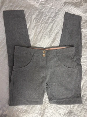 Grå leggings med fickor och knappar - Snygga grå leggings med två framfickor, två bakfickor och dekorativa träknappar framtill. Mjukt och stretchigt material som sitter skönt. Perfekta för en avslappnad och trendig look.