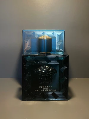 Versace Eros Eau de Parfum 100ml - Versace Eros Eau de Parfum i en lyxig, kvadratisk flaska i djup turkosblått glas med gulddetaljer och den ikoniska Medusa-symbolen i relief på framsidan. Flaskan har ett elegant mönster och ett matchande blått lock med guldkant. Parfymen är nästan ny då jag har använt den endast ett fåtal gånger. Finns en liten skada i nedre hörnet men påverkar inte produkten.