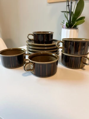 Fina koppar med fat från arabia - Säljer ett set med 5 bruna koppar och tillhörande fat i keramik. Från märket Arabia. Kopparna har en rund form med breda handtag och en glansig yta i mörkbrunt med olivgröna toner. Perfekt för fika eller te. Klassisk retrostil som passar i de flesta kök. Köpta vintage och efter lite sökande tror jag de är från 60-talet💕 helt felfria💕