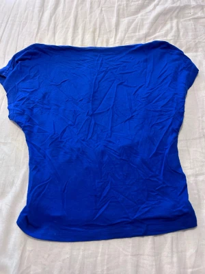 Kornblå topp med öppen rygg - Snygg kornblå topp i mjuk bomull med korta ärmar och en djup, öppen rygg. Perfekt för dig som vill ha en enkel men ändå iögonfallande look. Toppens passform är normal och materialet känns skönt mot huden.