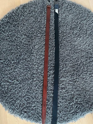 Två klassiska bälten i skinn - Säljer två stilrena bälten, ett i brunt och ett i svart skinn. Båda har enkel, rak design med silverfärgat spänne. Perfekta för att lyfta vilken outfit som helst och passar till både jeans och kostymbyxor. Båda de är från Dressmann. Båda kostar 500kr om man vill köpa ett bälte kostar det 275kr.