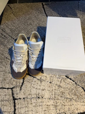 Maison Margiela sneakers - Maison Margiela sneakers i färgen vit med marinblå färg stänk på tå. Box och tags och allt orginalt tillkommer.