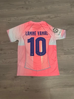 FC Barcelona rosa str S och M - Säljer en FC Barcelona matchtröja i rosa och ljusblått med Lamine Yamal och nummer 10 på ryggen. Tröjan har Champions League-märke på ärmen, Nike-logga och Spotify-logga på bröstet. Korta ärmar och sportig passform, perfekt för fotbollsträning eller support.
