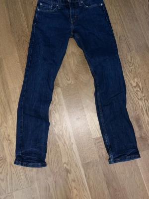 Mörkblå Levi's jeans straight fit - Snygga mörkblå jeans från Levi's med klassisk femficksdesign och raka ben. Jeansen har tydliga kontrastsömmar och en ikonisk läderpatch bak i midjan. Perfekta för en stilren och avslappnad look.