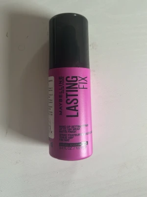 Maybelline Lasting Fix Face Mist - En rosa face mist från Maybelline med svart lock. Lasting Fix är en make-up setting spray som ger en matt finish och håller sminket på plats upp till 16 timmar. Flaskan rymmer 100 ml och är perfekt att ha i väskan för en fräsch look hela dagen.