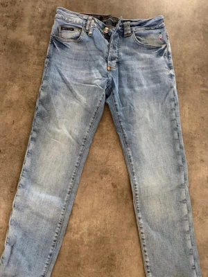 Ljusblå slim fit jeans från philipp plein  - Snygga ljusblå slim fit jeans från philipp plein   klassisk femficksdesign och diskreta slitningar. Jeansen har normal midja, dragkedjegylf och läderpatch med logga bak. Perfekta för en avslappnad och trendig look.