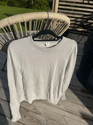 Ljusgrå stickad tröja från H&M - En stilren ljusgrå stickad tröja från H&M med rund halsringning och långa ärmar. Tröjan har en enkel och klassisk design som passar perfekt till olika outfits. Tillverkad i mjukt material för en bekväm känsla.