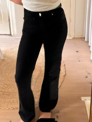 Svarta bootcut jeans med hög midja - Säljer ett par svarta bootcut jeans med hög midja och klassisk femficksmodell. Jeansen har en snygg, utsvängd passform och stängs med knapp och dragkedja. Perfekta till en enkel topp eller hoodie.