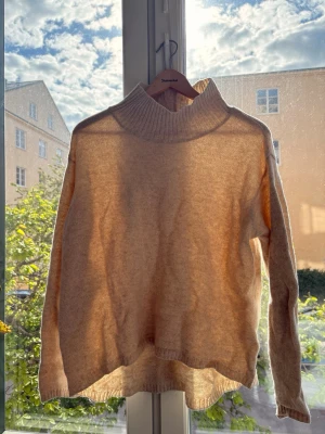 Beige stickad tröja Holebrook - Mysig beige stickad tröja från Holebrook Sweden med hög, ribbad polokrage och långa ärmar. Tröjan har en avslappnad passform och är perfekt för kyliga dagar. Materialet känns mjukt och skönt mot huden.
