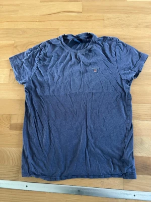 Blå t-shirt från Gant - En klassisk blå t-shirt från Gant med rund halsringning och liten broderad logga på bröstet. Tillverkad i mjuk bomull och har en normal passform. Perfekt till jeans eller shorts för en avslappnad look.