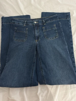 Blåa wide leg jeans med hög midja - Säljer ett par blåa wide leg jeans med hög midja och raka ben. Jeansen har klassiska fickor fram och bak, samt synliga sömmar i kontrastfärg. Perfekta för en avslappnad och trendig look. Materialet är klassisk denim och är stretchiga, passar påde S och M. Sitter perfekt över rumpan. 