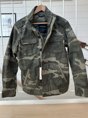 Field jacka camo - Mycket fet field jacka i tyg med camo mönster, perfekt för vår och sommar väder. Helt ny, aldrig använd, skick 10/10. Säljer då den är för liten för mig och jag missade returdatum. Skriv vid frågor eller funderingar!!