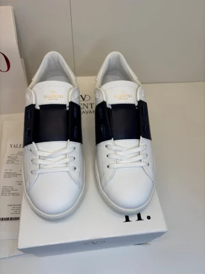 Valentino Opens 42 - Säljer ett par stilrena Valentino Garavani sneakers i vitt med marinblå detalj, storlek 42. Tidlös modell som passar till allt. Använda med normalt slitage på sulan (se bilder), men i fint skick i övrigt. Originalbox och kvitto medföljer. Äkta vara – bra pris jämfört med nypris! ✨