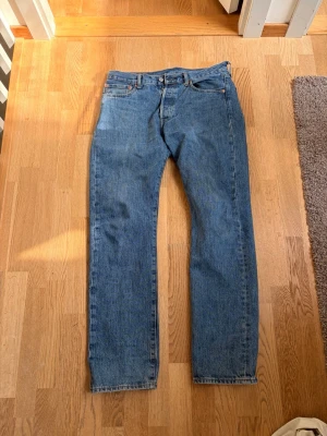 Levi's blå raka jeans (32:32) - Klassiska blå jeans från Levi's med rak passform. Jeansen har en ikonisk läderpatch bak i midjan och är tillverkade i slitstark denim. Perfekta för en avslappnad och tidlös stil.