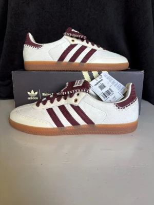 Adidas Samba x Wales Bonner Pony Tonal Cream White - Säljer ett par 100 % äkta, helt nya och oanvända Adidas Originals x Wales Bonner Samba "Pony Tonal Cream White" (Artikelnummer: IE0586). Modellen är Unisex och storleken är 8 UK / 8.5 US (motsvarar ca storlek 42). Dessa extremt eftertraktade skor har en unik ovandel i gräddvit fuskpäls/ponnyhår med vinröda detaljer. Allt är helt komplett och kommer med originalkartong (inklusive bottenplatta), tillhörande mönstrad dustbag samt extra skosnören. Säljes för ett bra pris vid snabb och smidig affär. 
