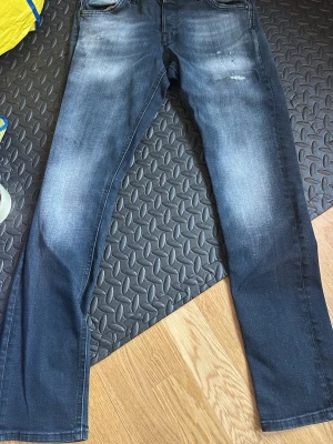 Mörkblå/grå slim fit jeans - Snygga mörkblå/grå slim fit jeans med lätt slitning på låren och klassiska fem fickor. Jeansen har en modern tvätt och raka ben, perfekta för en trendig vardagslook. Materialet är troligtvis bomull med lite stretch för extra komfort.