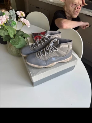 Grå Air Jordan 11 sneakers - Säljer ett par grå Air Jordan 11 sneakers med högt skaft och klassisk design. Skorna har en kombination av mocka och läder med ljusgrå detaljer och vita skosnören. Perfekt för dig som gillar ikoniska basketskor och streetstyle.