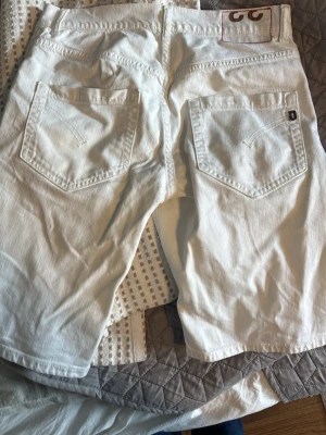 Vita jeansshorts från dondup  - Säljer ett par vita jeansshorts från dondup  med klassisk femficksdesign och knappgylf. Shortsen har raka ben och tydliga bakfickor med dondups  signaturdetaljer. Perfekta för en avslappnad och stilren look.