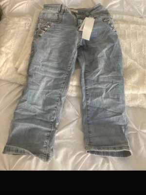 Ljusblå jeans med knappar i sidan - Snygga ljusblå jeans med raka ben och dekorativa silverfärgade knappar längs fickorna på sidorna. Jeansen har klassisk femficksdesign och är tillverkade i denim. Perfekta för en trendig och avslappnad stil.