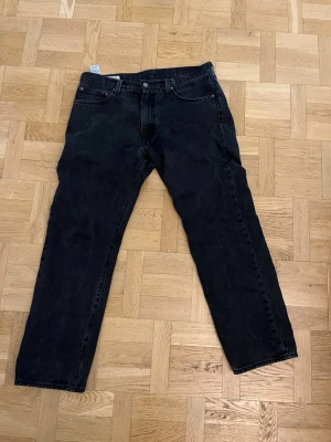 Svarta raka jeans från Levi's - Säljer ett par svarta jeans från Levi's med klassisk rak passform. Jeansen har fem fickor, knappgylf och diskret Levi's-märke på bakfickan. Tillverkade i slitstark denim med en mörk tvätt. Perfekta för en avslappnad och stilren look.