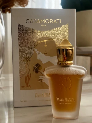 Casamorati Dama Bianca Eau de Parfum - Toppnoter: Lime, Kumquat Hjärtnoter: Italienska Iris, Egyptisk Jasmin, Lilja Basnoter: Sandelträ, Ceder, Vanilj, Ambrette (Musk Malva), Vit Musk, Malt