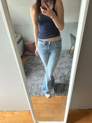 Ljusblå bootcut jeans - Säljer ett par ljusblå bootcut jeans med klassisk femficksdesign och låg midja. Jeansen har en snygg tvätt och är tillverkade i denim med lite stretch för extra komfort. Perfekta för en avslappnad och trendig look.