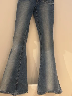 Blå utsvängda jeans från Gina Tricot - Snygga blå jeans från Gina Tricot med utsvängda ben och klassisk femficksmodell. Jeansen har en ljus tvätt och markerade sömmar, perfekta för en trendig och avslappnad look. Materialet är mjukt denim som sitter skönt hela dagen.