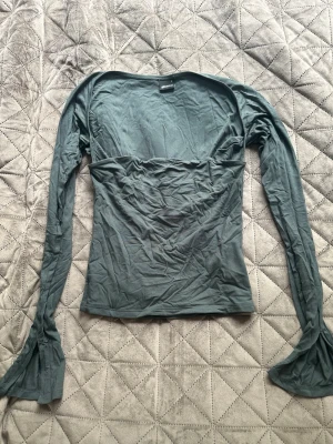 Grå/grön långärmad topp från Gina Tricot - Snygg grå/grln långärmad topp från Gina Tricot med figurnära passform. Toppen har utsvängda ärmslut och en enkel, stilren design som passar perfekt till jeans eller kjol. Tillverkad i mjukt material för en bekväm känsla.