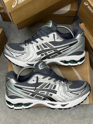 ASICS Gel-Kayano 14 silver/svart - Snygga ASICS Gel-Kayano 14 sneakers i silver och svart med gröna detaljer. Ovandel i mesh och syntet, klassisk ASICS-logga på sidan och chunky sula med gel-dämpning. Perfekta för dig som gillar sportig och trendig stil.