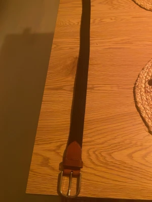Svart flätat bälte med bruna detaljer - Snyggt svart flätat bälte med bruna skinn-detaljer och silverspänne. Perfekt accessoar för att lyfta din outfit med en klassisk touch. Passar till både jeans och chinos.