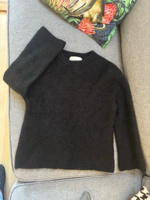 Svart stickad tröja från Ellos - Kashmir mohair Mysig svart stickad tröja från Ellos med rund halsringning och lång ärm. Tröjan har en fluffig och mjuk känsla, perfekt för kyliga dagar. Enkel och stilren design som passar till det mesta.