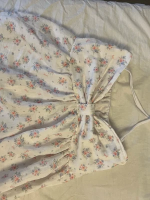 Blommig vit linnetopp - Supersöt vit linnetopp med små blommor i rosa och blått. Toppen har resår vid ryggen för extra komfort så att den inte åker ner i bak🤗 Toppen har tunna band som man knyter runt nacken och har en luftig passform. Perfekt för varma dagar och ger en romantisk vibe. Toppen har även dubbel tyg vid bysten som ger extra skydd för att man inte ska kunna se igenom🤗