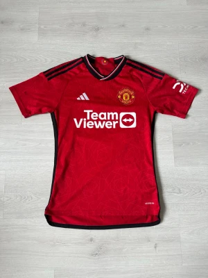 Manchester United S - Säljer en snygg och stilren Manchester United-tröja i fint skick och som är köpt utanför ARENAN! – perfekt för både matchdagar och vardagsstil! 🔴⚽ Tröjan är bekväm, av hög kvalitet. Passa på att uppdatera din supporter-garderob eller ge bort en uppskattad present till någon som älskar fotboll!  👉 Kika gärna in min profil – jag säljer fler fotbollströjor i olika modeller och storlekar. 💥 Rabatt erbjuds vid köp av flera plagg!  Hör av dig vid frågor eller intresse! 