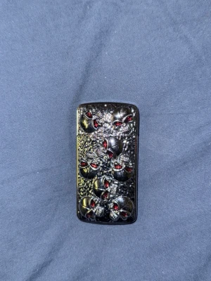 Svart zippo med dödskallemotiv - Unik svart tändare i metall med detaljerat dödskallemotiv och röda ögon på framsidan. Tändaren har en robust känsla och en cool, mörk design som sticker ut. Perfekt accessoar för dig som gillar alternativa eller rockiga stilar.