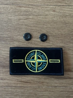 Stone Island patch med knappar - Säljer en klassisk svart Stone Island patch med gult och grönt broderat kompassmärke. Två svarta knappar medföljer perfekt om du tappar bort din patch! 
