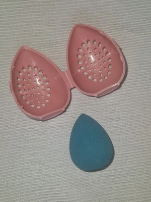 Beautyblender med etui - Blå beautyblender med ett rosa ventilerat etui i plast. Perfekt för att applicera foundation eller concealer och förvara svampen hygieniskt. Materialet på svampen är mjukt och flexibelt, medan etuiet är hårdplast med hål för ventilation. Helt nytt!