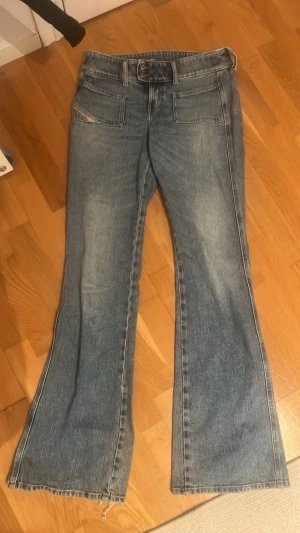 Blå bootcut jeans från diesel - Säljer ett par klassiska blå bootcut jeans från diesel med slitna benslut. Jeansen har låg midja, dragkedja och knapp snett vid midjan. Perfekta för dig som gillar en vintage och cool stil💕