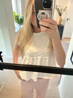 Vit volangblus med kort ärm - Supersöt vit blus med volangdetalj och korta ärmar. Modellen är luftig och har en avslappnad passform med en söt rynkad söm under bysten. Perfekt att styla med jeans eller kjol för en fräsch look.